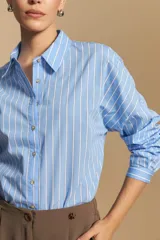 Camisa de manga larga a rayas verticales blancas y azules, con cuello camisero, cartera frontal con botones y calce relajado.