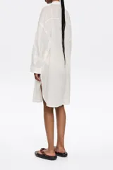 Vestido camisero de manga larga, corte oversize y largo midi, con estampado de mapa o temática náutica en tonos claros. Presenta cuello camisero, botonadura frontal y bolsillo plastrón en el pecho.