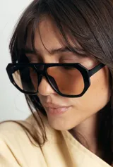 Lentes de sol con armazón de policarbonato negro y cristales tonalidad ámbar, con diseño de puente doble estilo aviador.