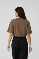 Remera de algodón color marrón con cuello redondo y mangas cortas. Presenta un estampado frontal con ilustraciones de dos copas de cóctel decoradas con lazos.