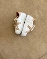 Sneakers de mujer estilo deportivo y urbano, color negro con detalles en beige claro. Presentan puntera y talón en negro, cuerpo principal en negro, y estrella lateral, cordones y tira de velcro en beige claro. La suela es blanca y el interior negro con la inscripción "LUCY IN THE SKY".