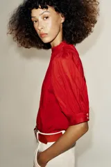 Blusa blanca de cuello alto con detalles de puntilla, manga corta abullonada y cierre posterior con botón.