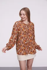 Blusa marrón con estampado de flores color naranja y blanco, con cuello redondo con abertura y mangas largas abullonadas.