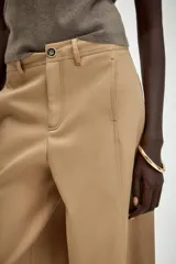 Pantalón de sarga en color beige, con tiro medio, cintura con trabillas y pernera recta. Presenta bolsillos de vivo en el delantero, cierre frontal con cremallera y botón metálico.