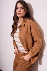 Sobrecamisa negra de estilo shacket, confeccionada en tejido de gamuza sintética. Presenta cuello camisero, cierre frontal de botones y dos bolsillos de parche con solapa en el pecho. El calce es oversize y las mangas son largas.