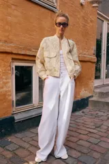 Chaqueta tipo bomber de cuello redondo y manga larga, confeccionada en tejido jacquard con diseño floral en tonos dorados y crema. Presenta cierre frontal con cremallera, bolsillos delanteros de plastrón con solapa y puños y bajo elásticos.