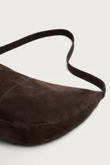 Bolso de hombro con diseño de media luna, confeccionado en piel con acabado de serraje. Cuenta con un asa integrada y cierre principal mediante cremallera.