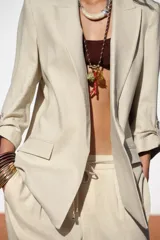 Blazer color beige confeccionada en lino, de corte recto, con cuello solapa, hombreras y mangas 3/4 con trabilla y botón dorado.