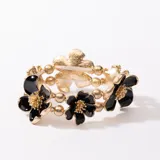 Pulsera elástica con doble hilera de cuentas doradas y flores de resina negra con centro dorado.