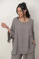 Blusa de lino color verde militar, holgada, de manga 3/4 con volados en los puños, cuello redondo y detalle de alforzas horizontales en el dobladillo.