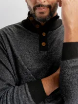 Buzo de punto con textura jaspeada, cuello alto y cierre frontal parcial con botones de madera. Presenta puños y cuello en tejido acanalado de color negro.