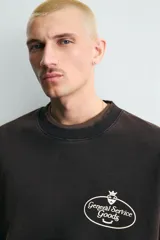 Sudadera de corte relajado color negro con efecto lavado, cuello redondo, manga larga y puños en rib. Presenta un estampado gráfico a contraste en el pecho con el texto 'General Service Goods'.