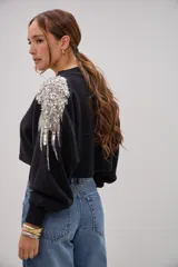 Sweater negro de corte cropped con detalle de apliques bordados en pedrería y lentejuelas plateadas sobre el hombro. Presenta mangas largas con puños ajustados y cuello redondo.