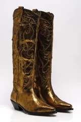 Bota alta estilo cowboy color dorado metalizado, con bordados decorativos y puntera en punta.