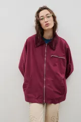 Campera de estilo urbano color bordó, con cierre frontal metálico, cuello de pana y bolsillo con cierre en el pecho. Presenta un diseño holgado y bolsillos laterales.