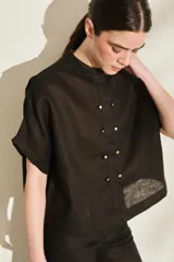 Blusa negra de lino de silueta amplia, con cuello mao y doble hilera de botones dorados en el frente. Cuenta con mangas cortas con vuelta.