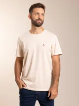 Remera básica de manga corta en color beige, confeccionada en algodón, con cuello redondo y pequeño logo bordado en color rojo en el pecho.