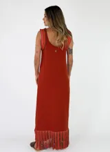 Vestido largo negro de punto con tirantes anchos rayados en tonos marrones y amarillos, escote redondo y flecos multicolor en el ruedo.