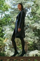 Blazer largo de eco cuero color negro, con solapas clásicas, cierre frontal con botones y diseño de corte recto.