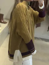 Buzo tejido de punto con cuello alto, diseño holgado y aberturas laterales. Presenta un cuerpo en color azul melange con detalles de franjas en color crema y verde en los puños y el ruedo. Incluye un pequeño bordado en el pecho.