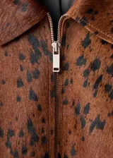 Chaqueta de cuero de potro color marrón con estampado tipo animal print en tonos oscuros, de corte recto y largo recortado. Cuenta con cuello camisero, cierre frontal de cremallera metálica y mangas largas amplias con puños rectos.