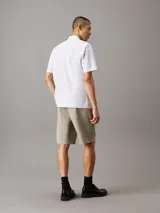 Camisa de manga corta Calvin Klein confeccionada en popelín de algodón elástico con diseño de rayas verticales. Presenta cuello en punta, cierre frontal de botones, bolsillo de parche en el pecho con logo bordado y bajo recto.