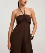 Mono largo de estilo Aladim, color marrón oscuro, con escote halter y busto fruncido. El pantalón es ancho y termina ajustado en los tobillos.