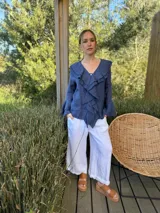 Camisa de lino azul marino con volados en cascada a lo largo del frente y en los puños de las mangas largas. Presenta un escote en V con un botón de nácar visible.