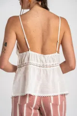 Top blanco de algodón peinado con tirantes finos, escote en V con detalle de encaje y cierre frontal abotonado. Presenta inserciones de encaje transparente en el abdomen y un diseño fluido en la parte inferior.
