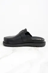 Zueco negro de cuero con hebilla metálica plateada ajustable y suela track.