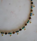 Collar de piedras semipreciosas de crisocola y ojo de tigre, con pequeñas cuentas doradas y dijes en forma de gota bañados en oro.