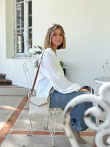 Cartera tipo sobre color crudo, confeccionada en cuero, con correa larga de cuero marrón y costuras decorativas en contraste.