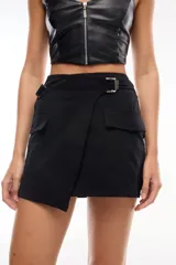Minifalda negra con cruce asimétrico, hebilla metálica lateral y bolsillos tipo cargo.