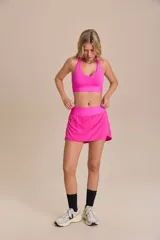 Pollera deportiva color rosa fucsia, con estampado en relieve de texto. Es de corte corto con ruedo redondeado y cuenta con shorts internos.