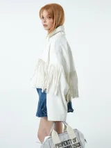 Chaqueta blanca de cuero sintético con cuello camisero, cierre frontal con botones a presión y detalle de flecos en el pecho y las mangas.