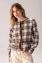Blusa de manga larga confeccionada en tartán con estampado a cuadros en tonos marrones, blancos y mostaza. Presenta detalles en cuero marrón y cuello alto con corderito sintético.