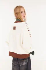 Sweater oversize de corte boxy, color crema con rayas verticales en tonos marrones y detalles de flecos colgantes. Presenta cuello redondo y puños y ruedo en tejido acanalado de color marrón oscuro.