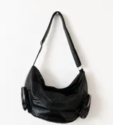 Cartera tipo hobo de cuero sintético color negro, con diseño espacioso y dos bolsillos laterales estilo cargo con cierre. Incluye correa ajustable para el hombro y bolsillo interno.