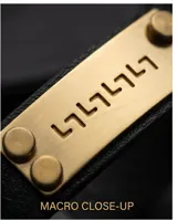 Pulsera de banda de cuero negro con placa central de acero en tono dorado, decorada con un diseño de guarda griega y remaches laterales. Cuenta con un cierre de seguridad de acero inoxidable.