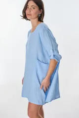 Vestido celeste de lino, con cuello redondo, corte oversize y mangas 3/4 con botón para enrollar.