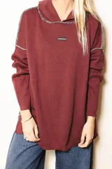 Sweater de punto color bordó con capucha, diseño holgado y costuras a contratono visibles en hombros y capucha. Presenta etiqueta con logo de la marca en el pecho.