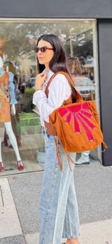 Cartera tipo tote bag confeccionada artesanalmente en cuero y gamuza, con diseño bicolor en verde y marrón. Presenta un detalle decorativo frontal con costuras a la vista en forma de abanico y flecos laterales. Es un modelo reversible con una cara lisa.