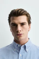 Camisa regular fit de algodón con diseño de rayas finas celestes y blancas. Cuenta con cuello abotonado, manga larga con puños abotonados y cierre frontal de botones.