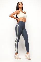 Calza deportiva de tiro alto en color azul grisáceo, con diseño de tres líneas verticales en color crema en los laterales. Confeccionada en tejido técnico de alta compresión, presenta un corte sin costura frontal para mayor comodidad.