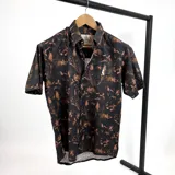 Camisa de manga corta negra con estampado de hojas marrones y logo bordado en el pecho.