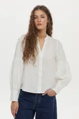 Camisa de lino color beige, con escote en V, cuello mao y mangas abullonadas tres cuartos. Cuenta con cierre frontal de botones y tiras ajustables para atar en la cintura.