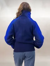 Chaqueta azul con mangas largas, cuello alto y cierre frontal con cordón. Diseño calado en el frente y mangas con patrón de rombos. Confeccionada en lana merino.