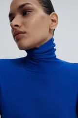 Jersey de punto liso en color beige, con cuello alto y manga larga con detalle de botones metálicos en los puños.