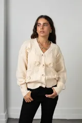 Saco de punto color manteca con cuello en V, cierre frontal de botones y apliques de flores bordadas en relieve. Presenta diseño de trenzas y puños acanalados.