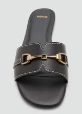 Sandalias planas de color negro con puntera redondeada, tira ancha con costuras blancas a contratono y detalle metálico dorado en el empeine.